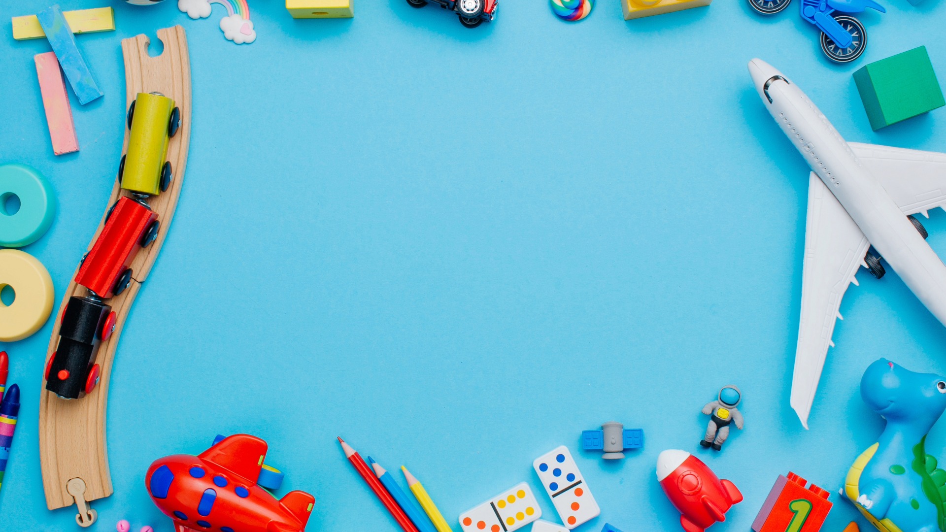 Spielzeugeisenbahn, Holzschienen, Spielzeugflugzeug, Dominosteine, Buntstifte und weitere bunte Kinderspielzeuge auf blauem Untergrund