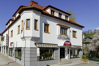 Eckgebäude mit weißer Fassade, mehreren Fenstern und rotem Markisenüberdach am Eingang bei klarem Himmel