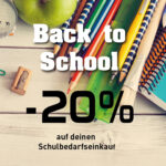 Bunte Schulutensilien mit Buntstiften, Lineal, Heften, Pinsel, Spitzer und Büroklammern auf einem hellen Holztisch.